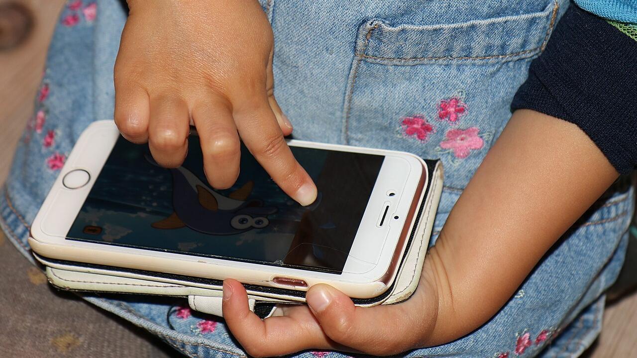 Eine Kinderhand tippt auf einem Smartphone